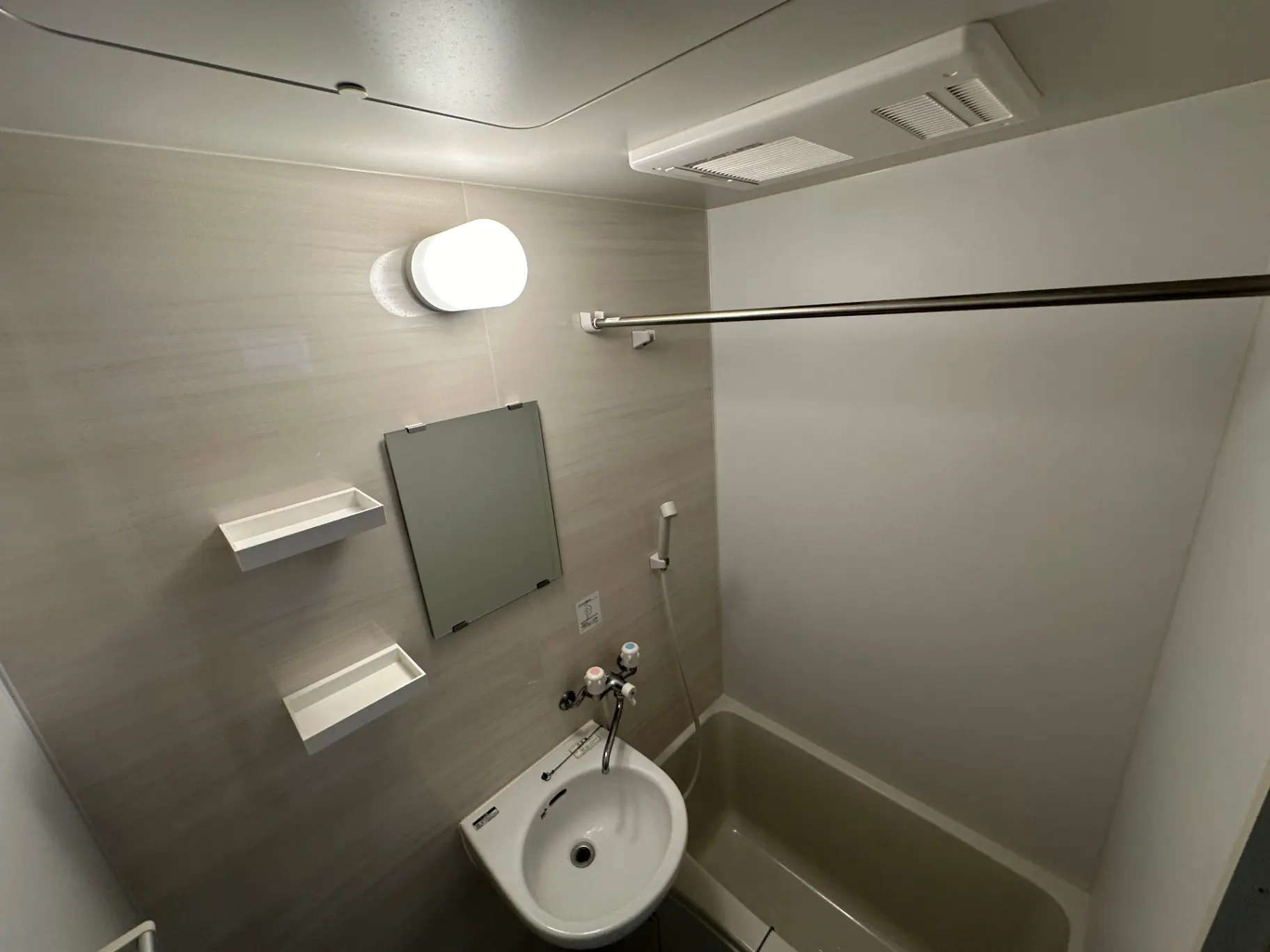 シンプルなデザインのトイレと洗面所、壁に取り付けられた棚とミラー、白い照明のモダンなバスルームインテリア