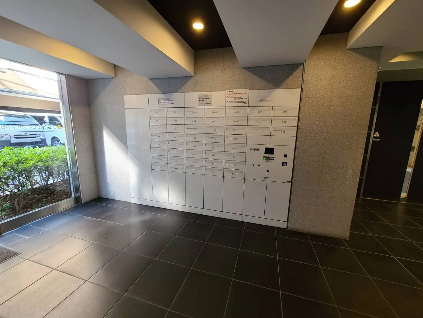 マンションのエントランスに設置された白い宅配ボックスと郵便受け、モダンなデザインの照明と床
