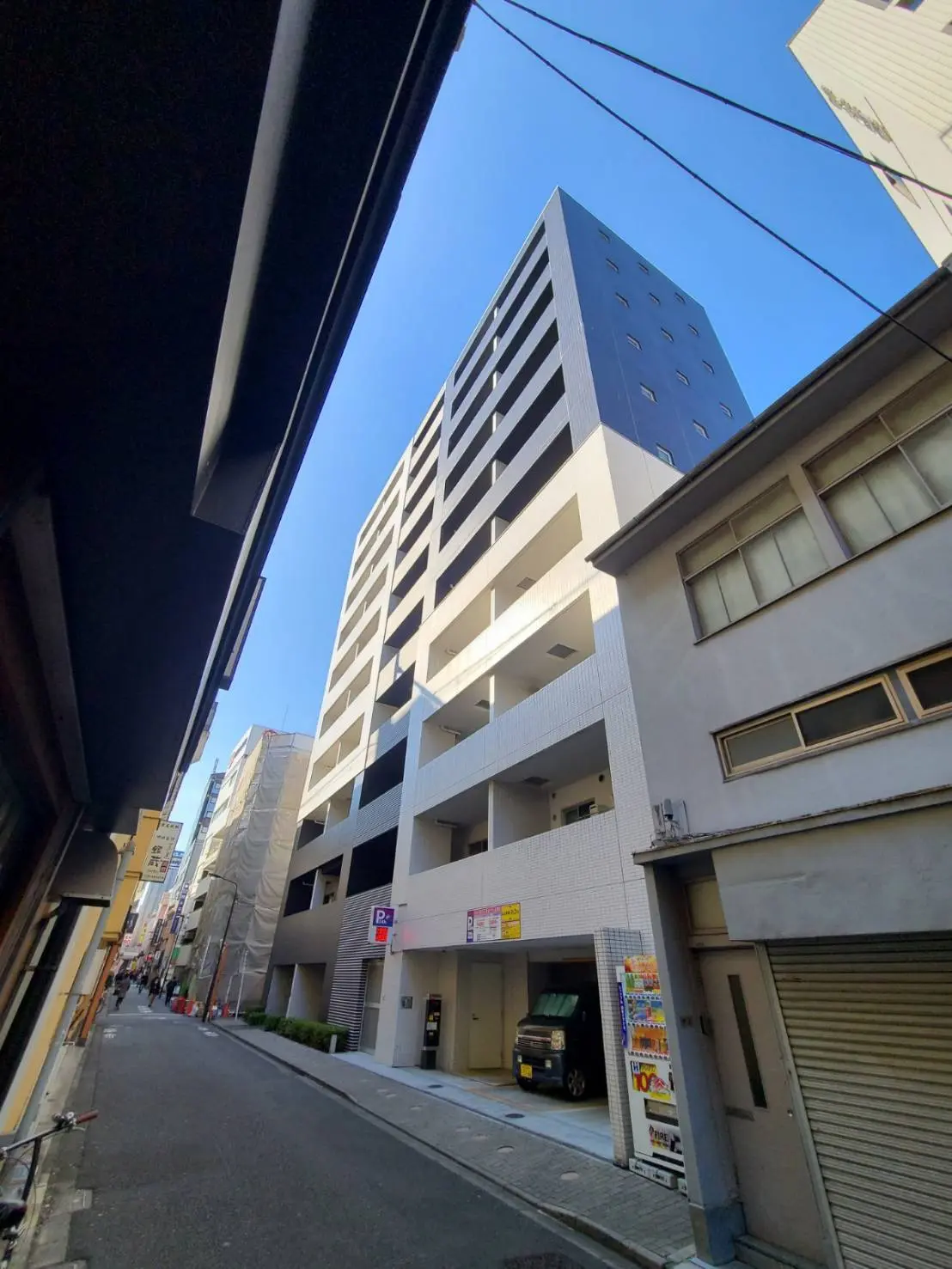 都心の狭い路地に立つモダンなデザインのマンションビル、青空と建物のコントラストが印象的な都市風景