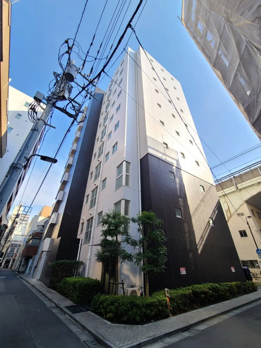都心にあるモダンな外観の高層マンション、青空と電線が交差する風景