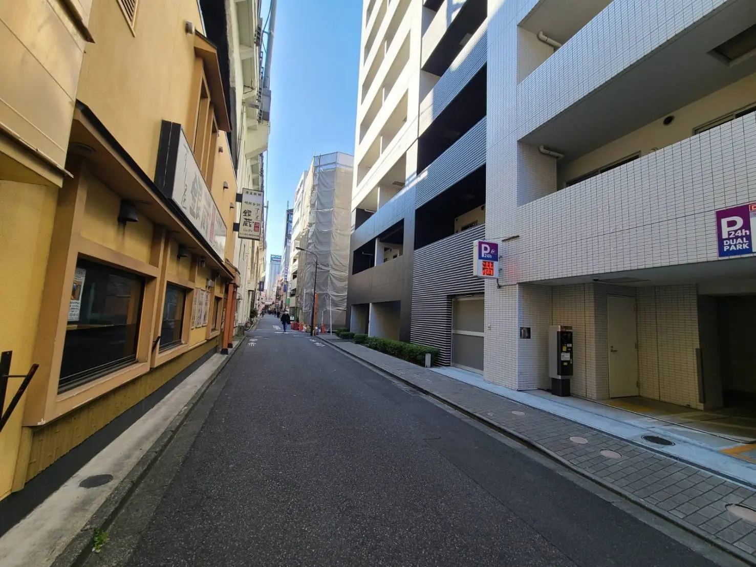 狭い路地の風景、左側に古い建物、右側に白いタイルのビルと駐車場入り口