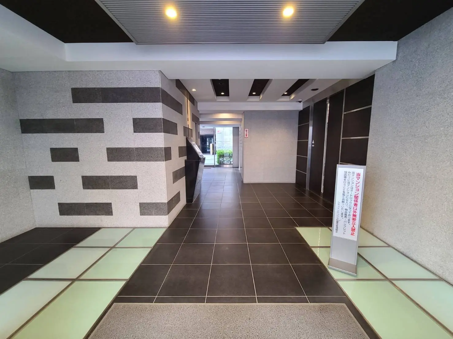 モダンなマンションのエントランスホール、モノトーンの壁デザインとタイルの床、綺麗な通路