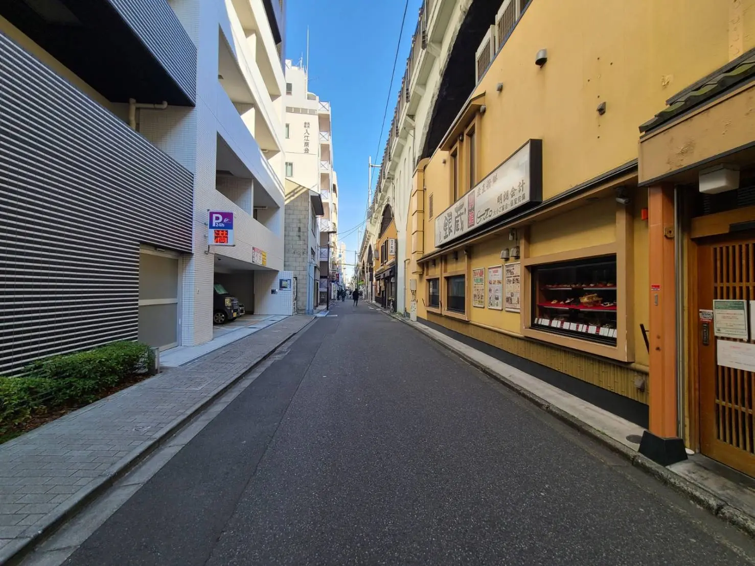 狭い都市の路地、昼間の日差し、右側に和食レストランの外観
