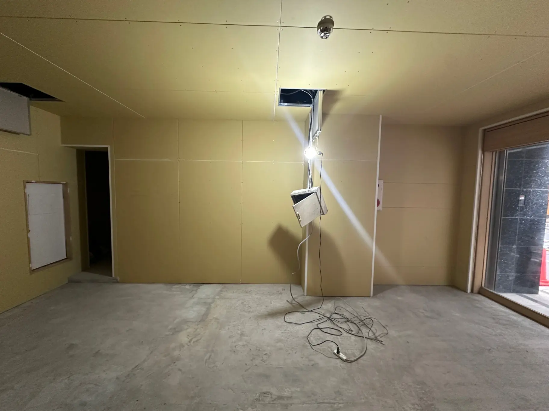 未完成の工事現場、壁紙が貼られていない壁と床、吊り下げられた電灯と配線が見えるインテリア