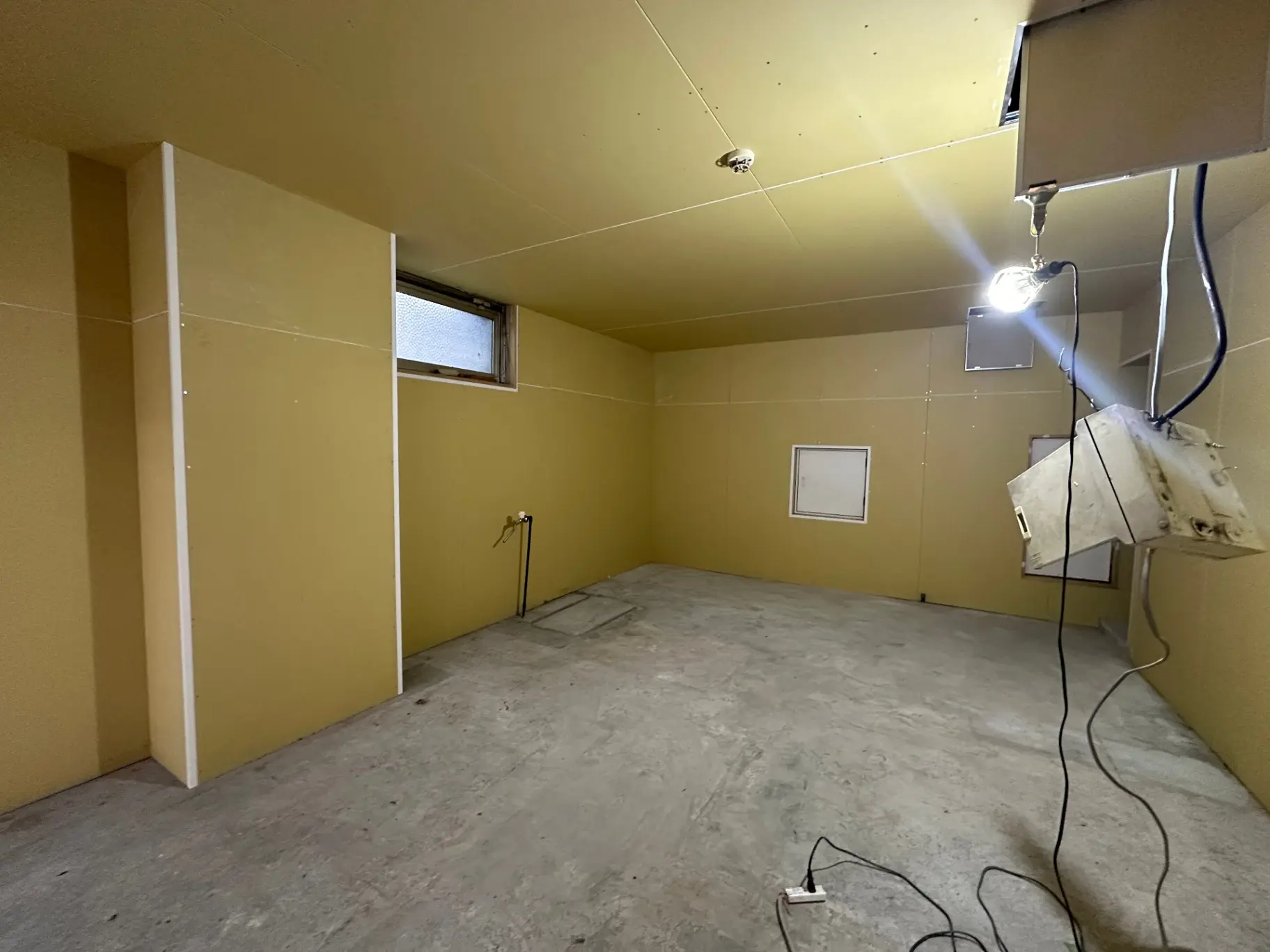 改装前の空き部屋、壁紙とコンクリートの床、電気工事中の照明と窓