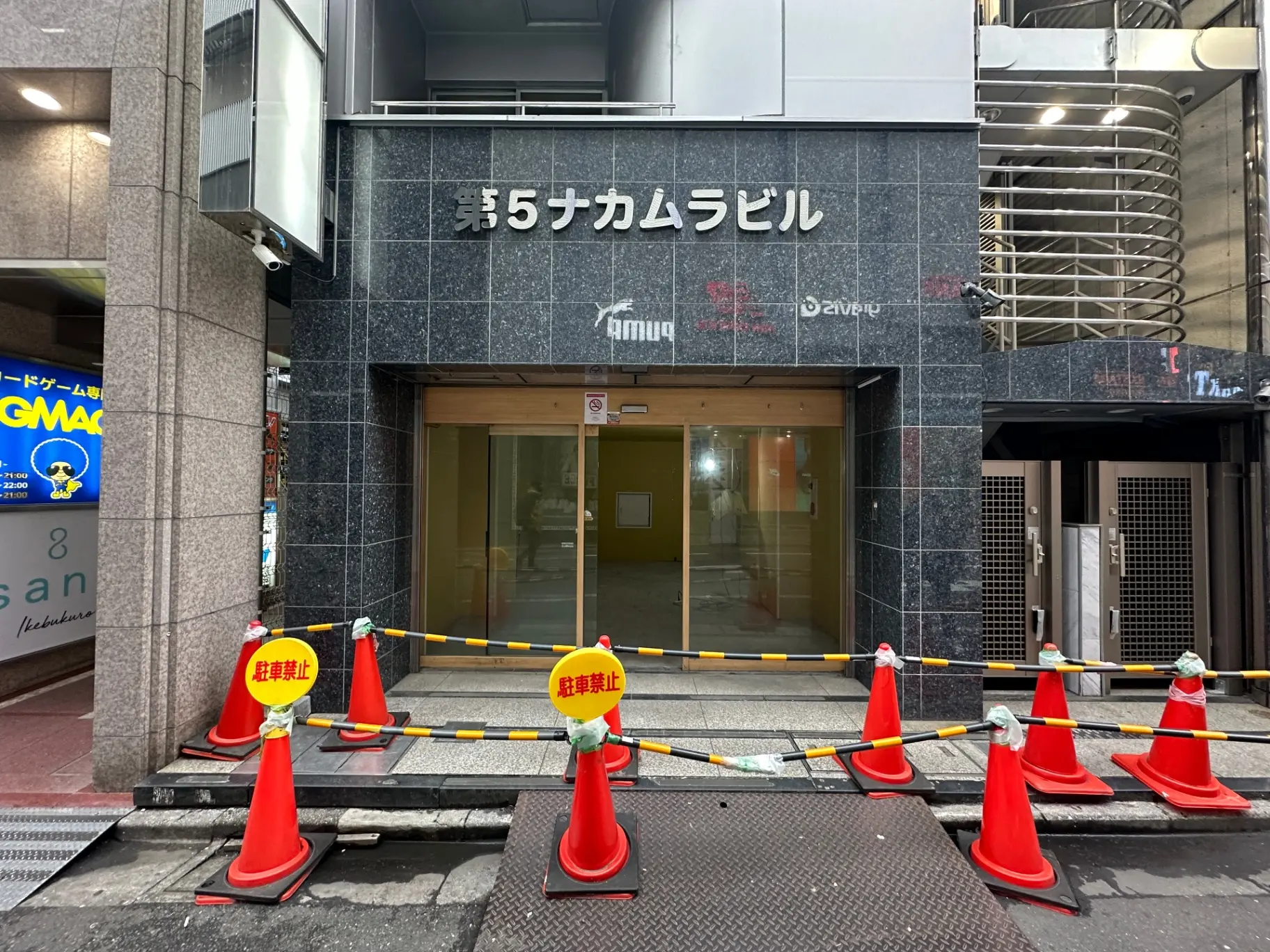 建物の入り口に設置された安全コーンとテープ、工事中の様子を示す注意看板があるストリートビュー