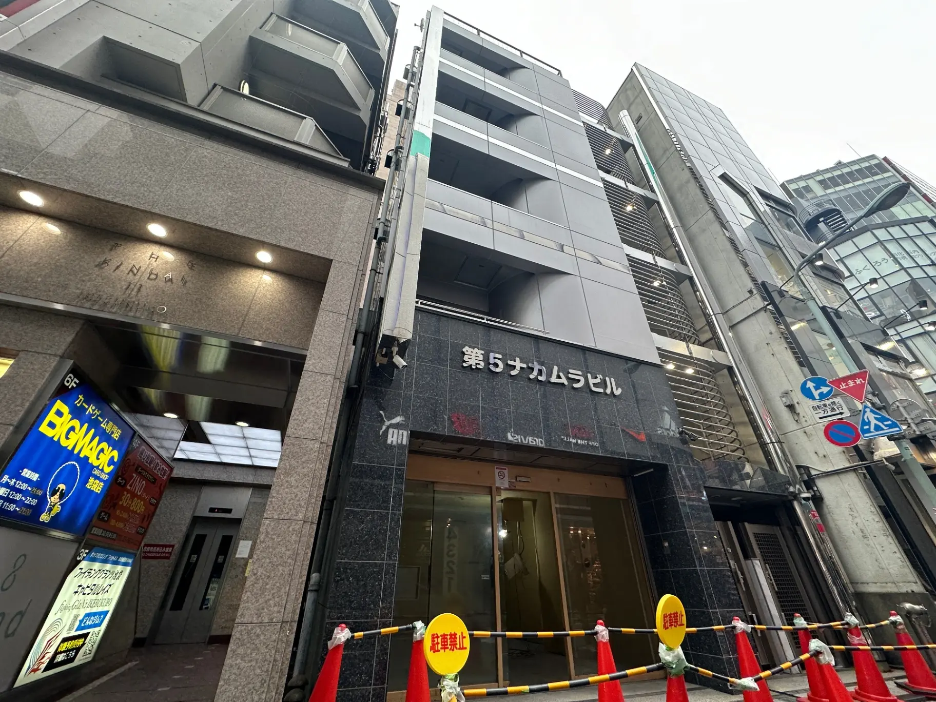 都会のビル街に位置するオフィスビルの外観、黒とグレーのモダンなデザインとガラス張りのエントランス