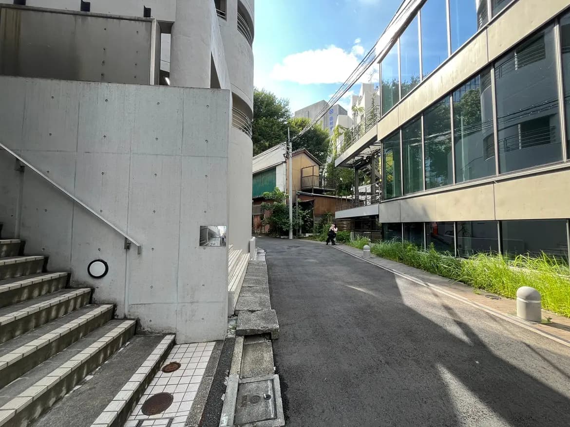 - 近代的なコンクリートの建物とガラス張りのファサード、階段横の手すり、周囲の緑と静かな通りの風景