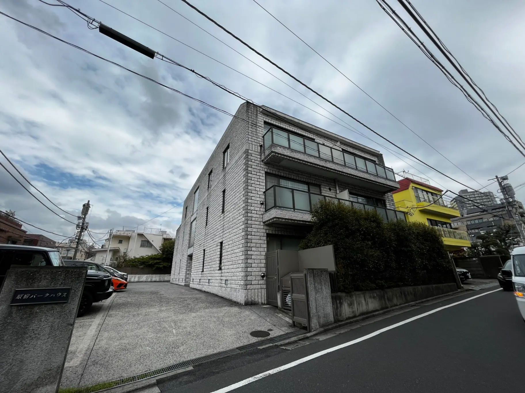 都会の住宅街に建つモダンな外観の白い壁のビルディング、周辺には色とりどりの建物が見える外観写真