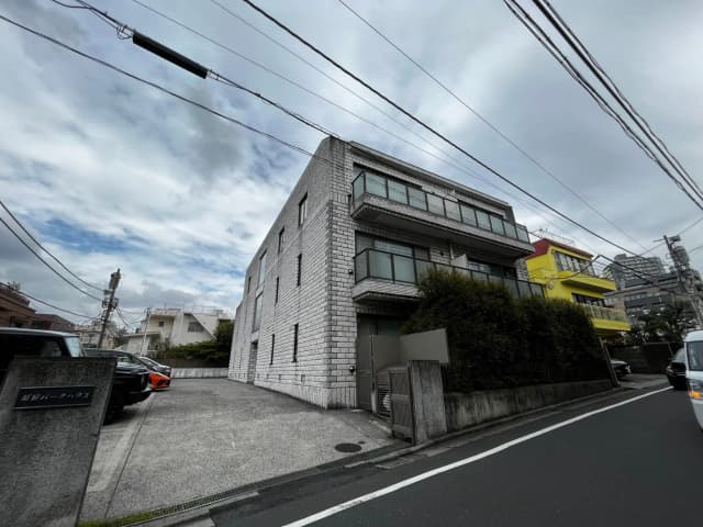 都会の住宅街に建つモダンな外観の白い壁のビルディング、周辺には色とりどりの建物が見える外観写真