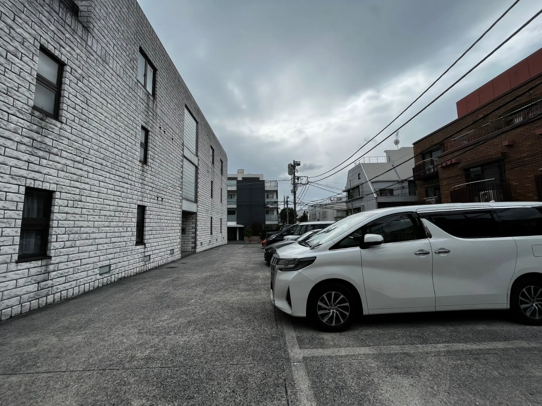 現代的な建築様式の都市風景、白い壁の建物と駐車されたミニバン、曇り空