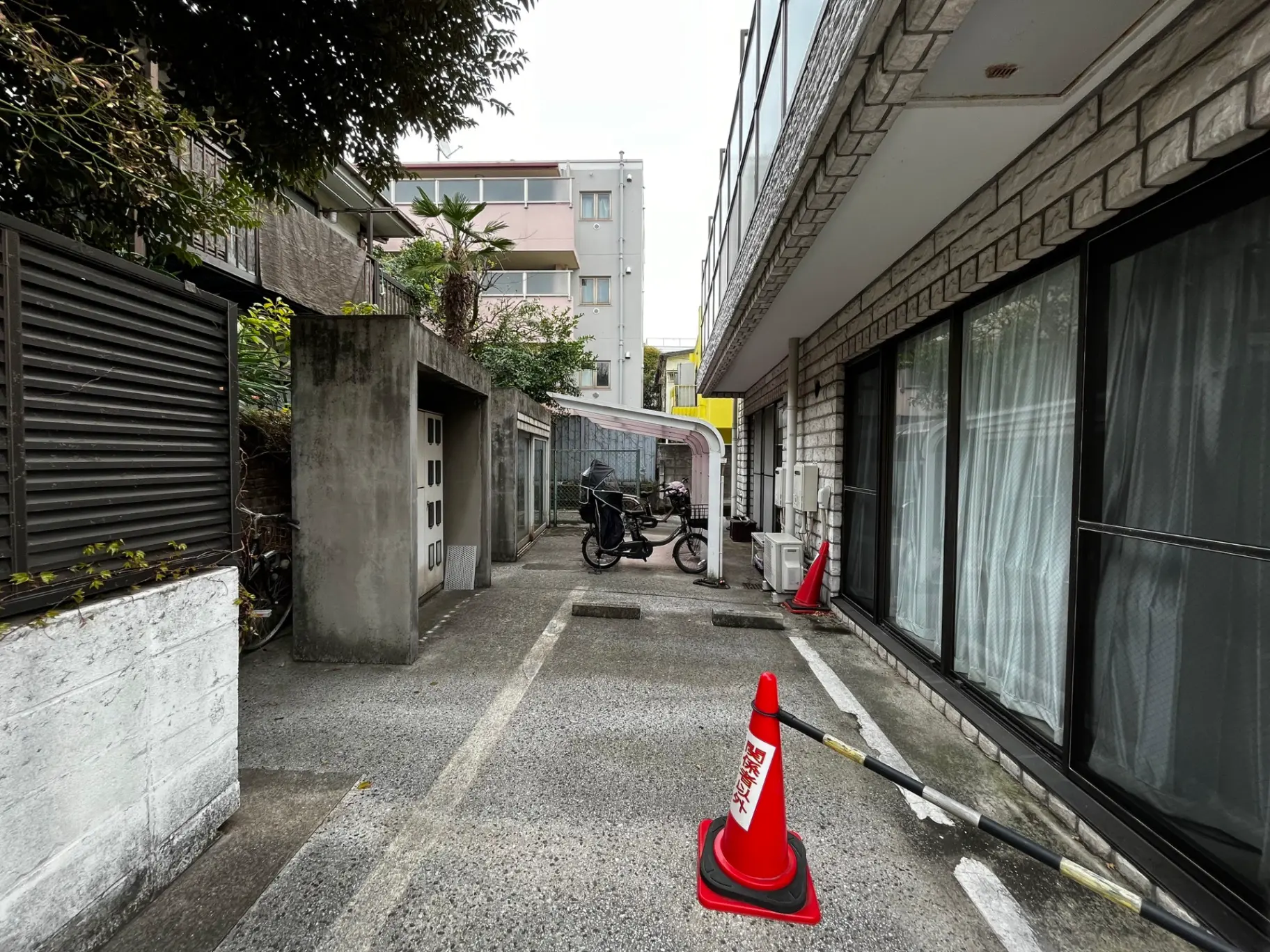 都市の住宅街の狭い路地、自転車が停まっている風景、建物の窓と渋い色合いの外壁