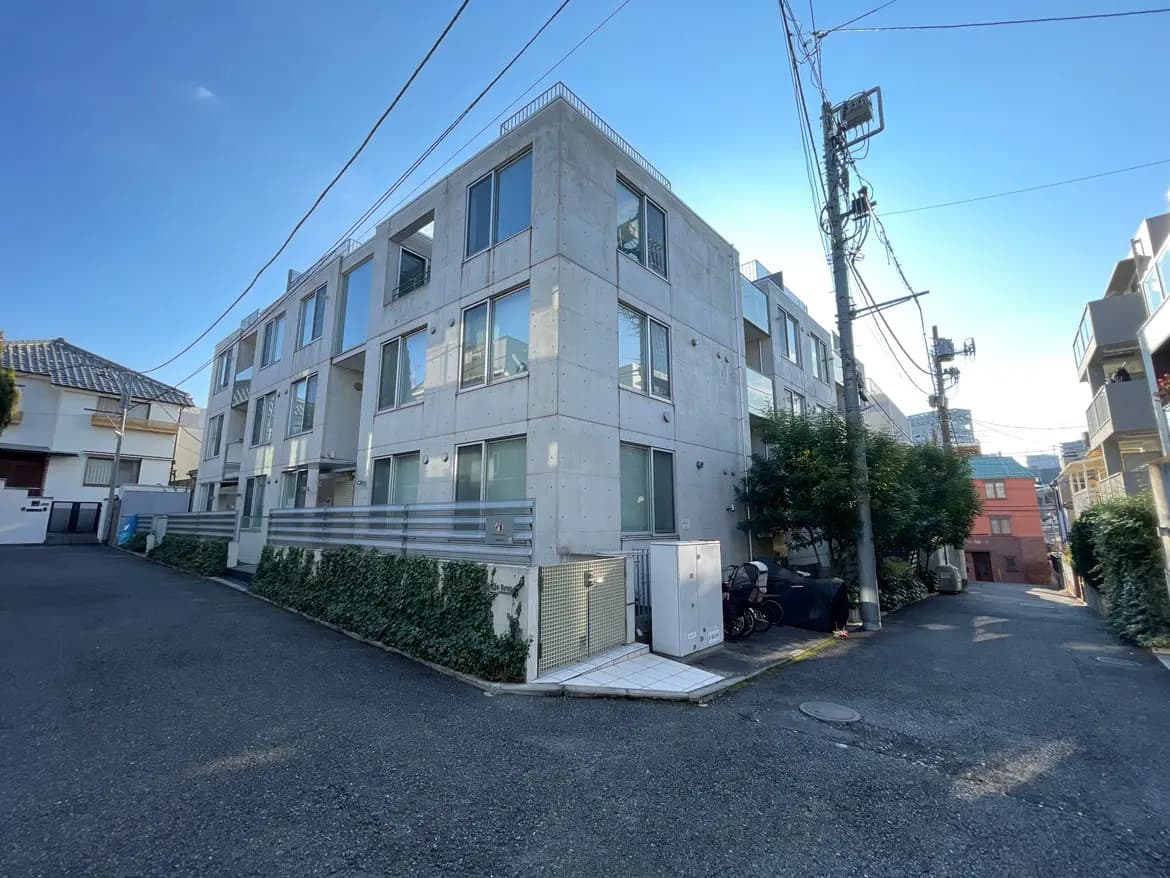 都市の住宅街にあるモダンな外観のアパートビル、晴れた日の木陰と青空
