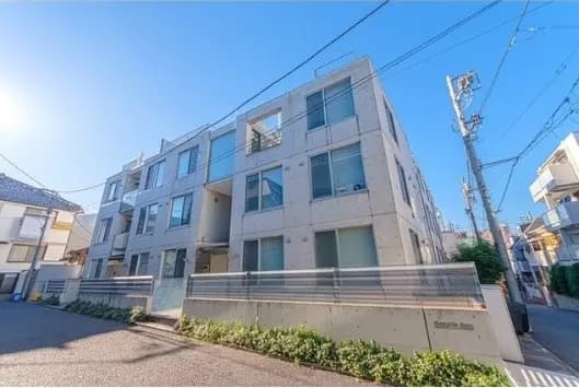都市の住宅街に立つモダンなデザインのマンション外観、晴れた日の青空と緑の植栽
