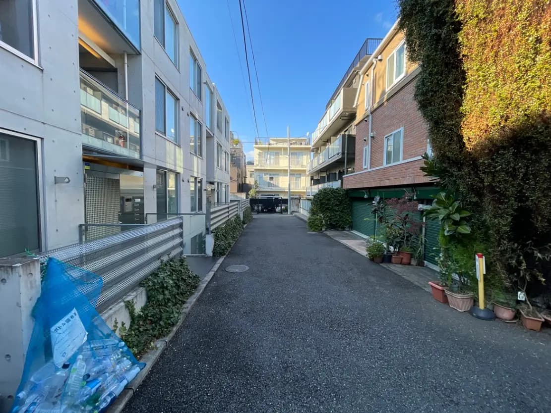 日中の住宅街、現代的なアパートと伝統的な家並み、清掃されたアスファルト道路と植物が並ぶ