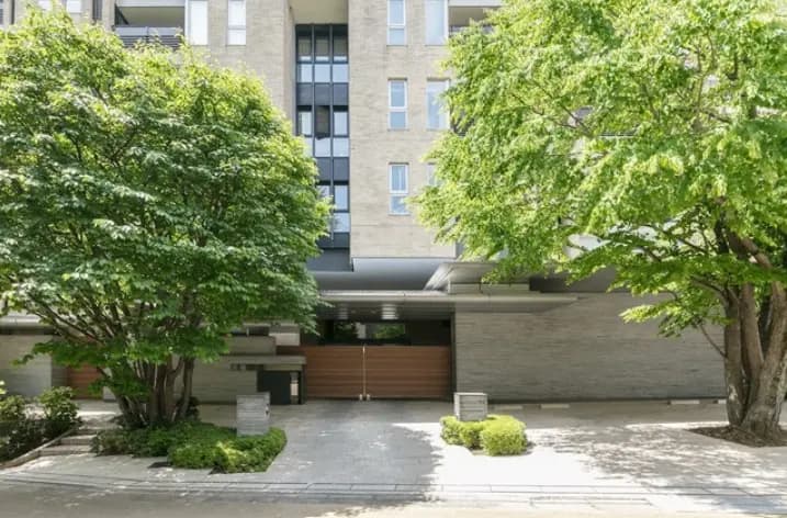 モダンで洗練された外観のマンションエントランス、緑豊かな樹木と石畳の通路