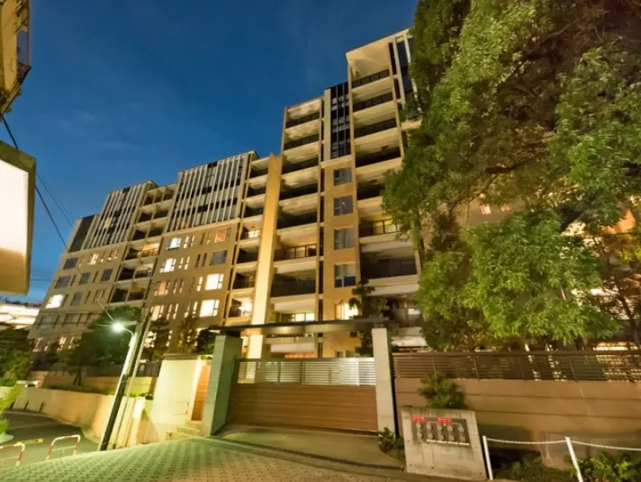 夜景を背景にライトアップされたモダンなマンションの外観、緑豊かな植栽と入り口の門扉