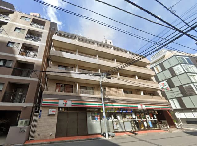 - 7-Elevenが入った住宅ビルの外観、左側に隣接した棟と青空の下で電線が張り巡らされた様子