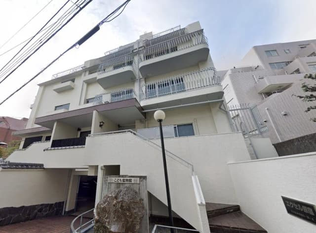 - 白い外壁の建物、バルコニーのある中層アパート、周囲に住宅街が広がる様子