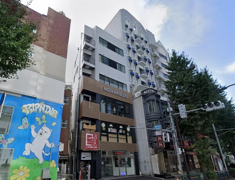 - ノデラビルの外観、ブルーのバルコニー、カラフルなアート壁面と周辺の緑豊かな街並み