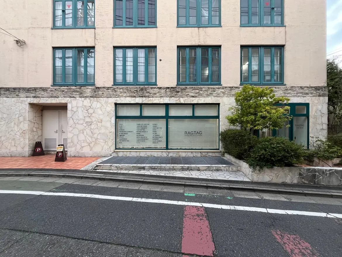 - 洗練されたデザインの商業施設の外観、緑の窓枠と石張りの壁、RAGTAGのロゴが見える店舗入り口