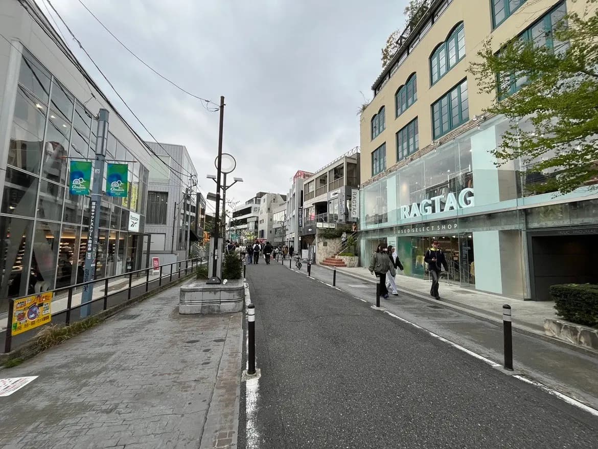 - 人々が行き交う活気ある商店街、RAGTAGの店舗がある通りの様子、モダンな建物と灰色の空が広がる風景