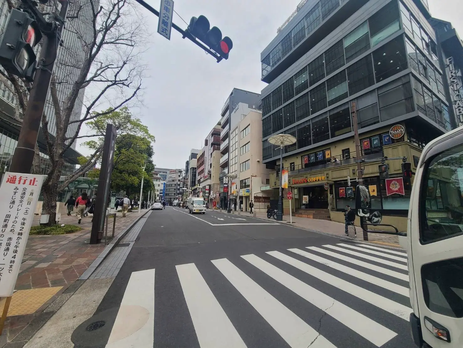 - 交差点の信号と横断歩道、大通り沿いの商業ビルやカフェ、歩行者が行き交う賑やかな街並み