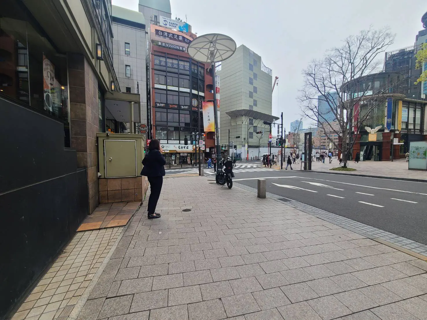 - 街角に立つ女性と周囲の商業ビル、交通が行き交う舗装された歩道の風景