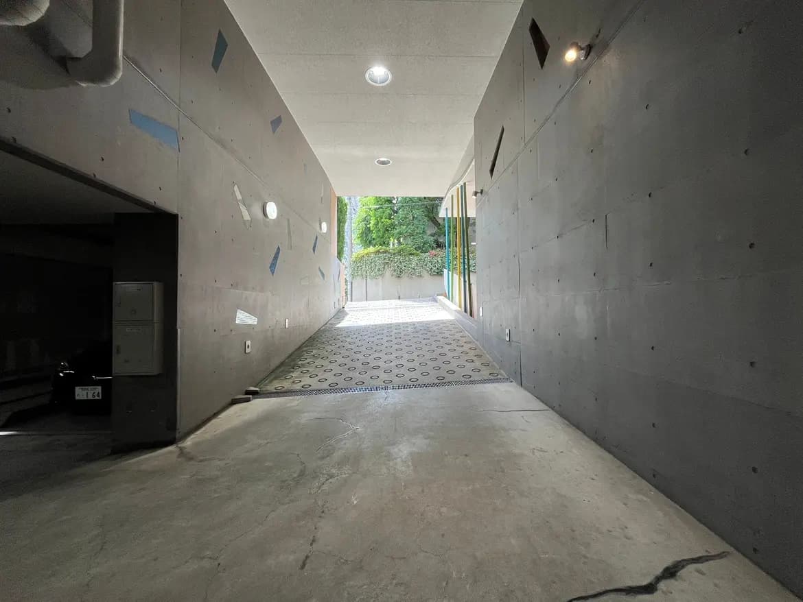 - 現代的なコンクリートの通路とガレージ、自然光が差し込む明るい空間、緑の景色が見える先端