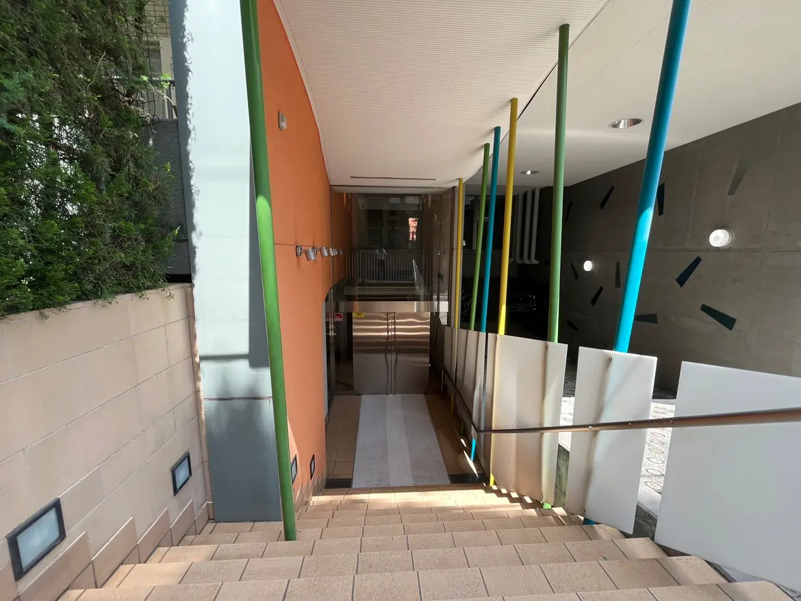 - カラフルな柱とモダンなデザインのエントランス、階段の周りには植物と滑らかなフローリングの通路が広がる空間