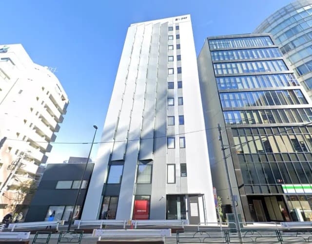 - 白い外壁のモダンなオフィスビル、隣にはガラス張りのビルと重厚感のある建物が並ぶ街並み