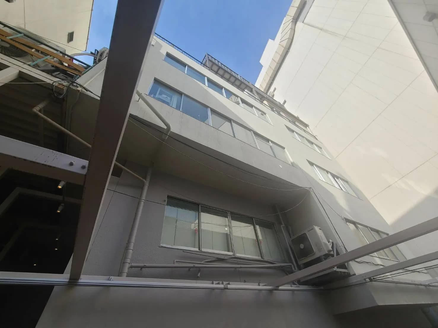 - ビルの外観、窓が並ぶ複数階の建物と青空が見える構図、空調設備の取り付けがある風景