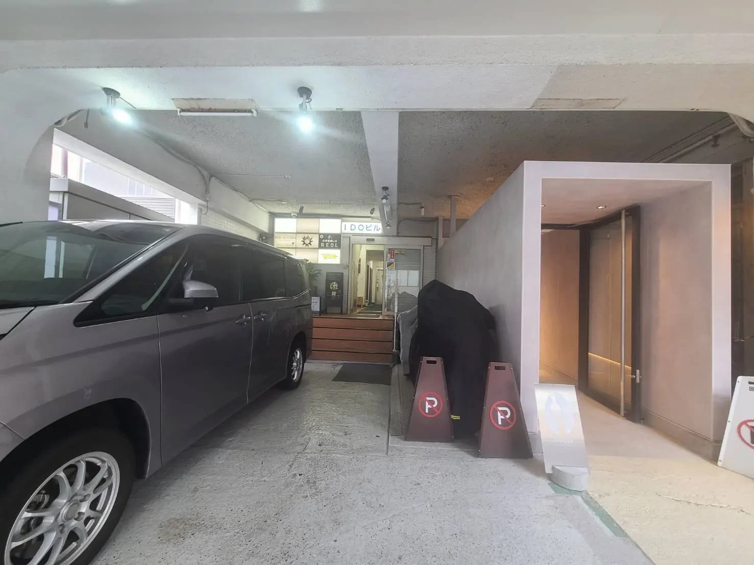 - 駐車場に停車したミニバンと明るい照明のエントランス、奥に見える受付と案内板がある現代的な入口の景観