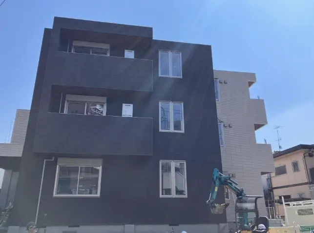 - モダンなデザインのブラックのアパートメント外観、バルコニーと大きな窓を持つ建物、隣に異なるカラーの建物がある景観