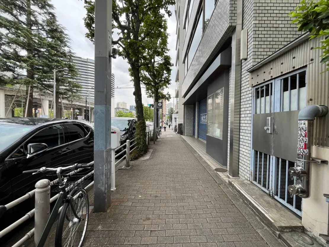 - 都会の通り沿いの歩道、自転車、黒い車並ぶ風景と緑の木々がある街並み