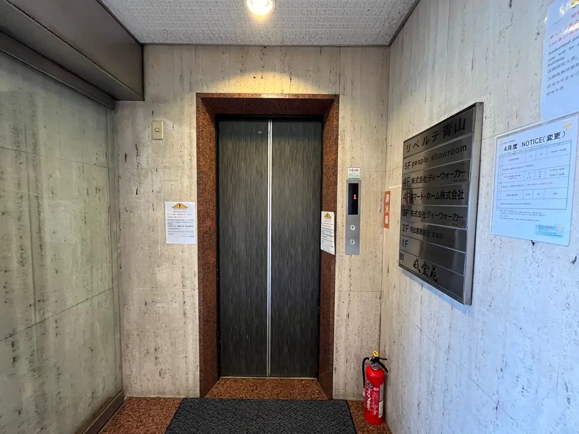 - エレベーターの前景、モダンな内装の壁、案内板や緊急設備が設置されたオフィスビルのエントランス