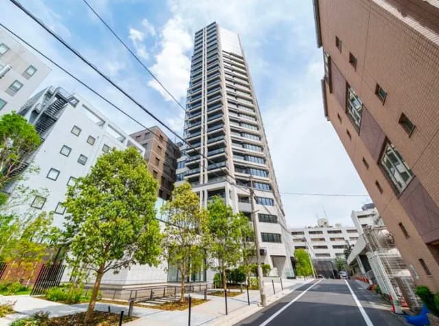 - 近代的な高層ビルと緑豊かな歩道、周囲に住宅が立ち並ぶ都市風景の写真