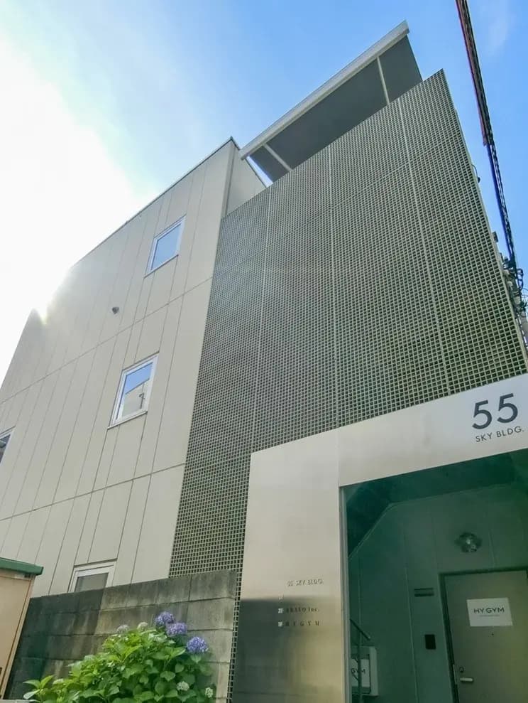 - 現代的なデザインの建物、グリッド状の外壁と「55 SKY BLDG」と書かれたエントランス、大きな窓と青空が広がる風景