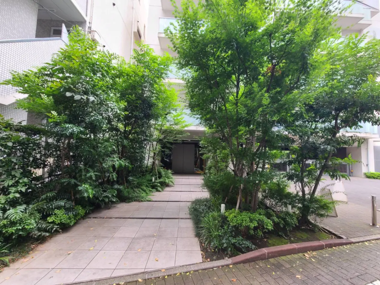 - 緑豊かな庭の中にあるエントランス、周囲に配置された植栽と整然とした石畳のアプローチ
