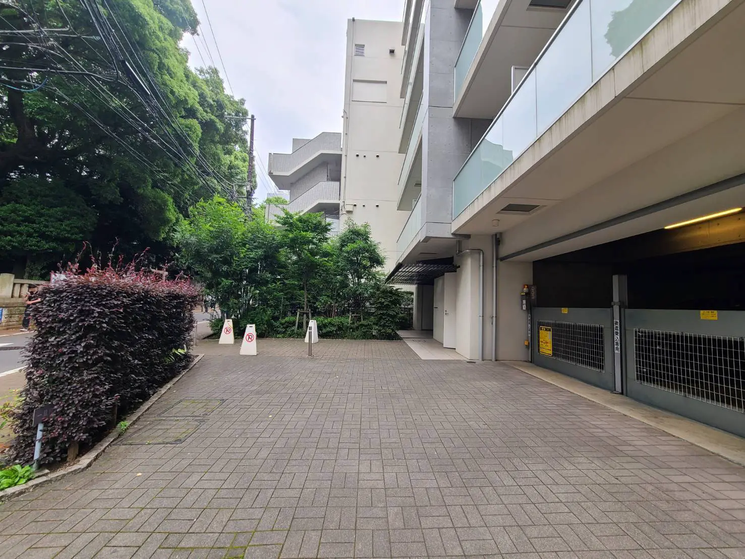 - 都市の住宅街に位置する駐車場、周辺には緑豊かな植物と舗装された歩道、低い建物が並ぶ景観