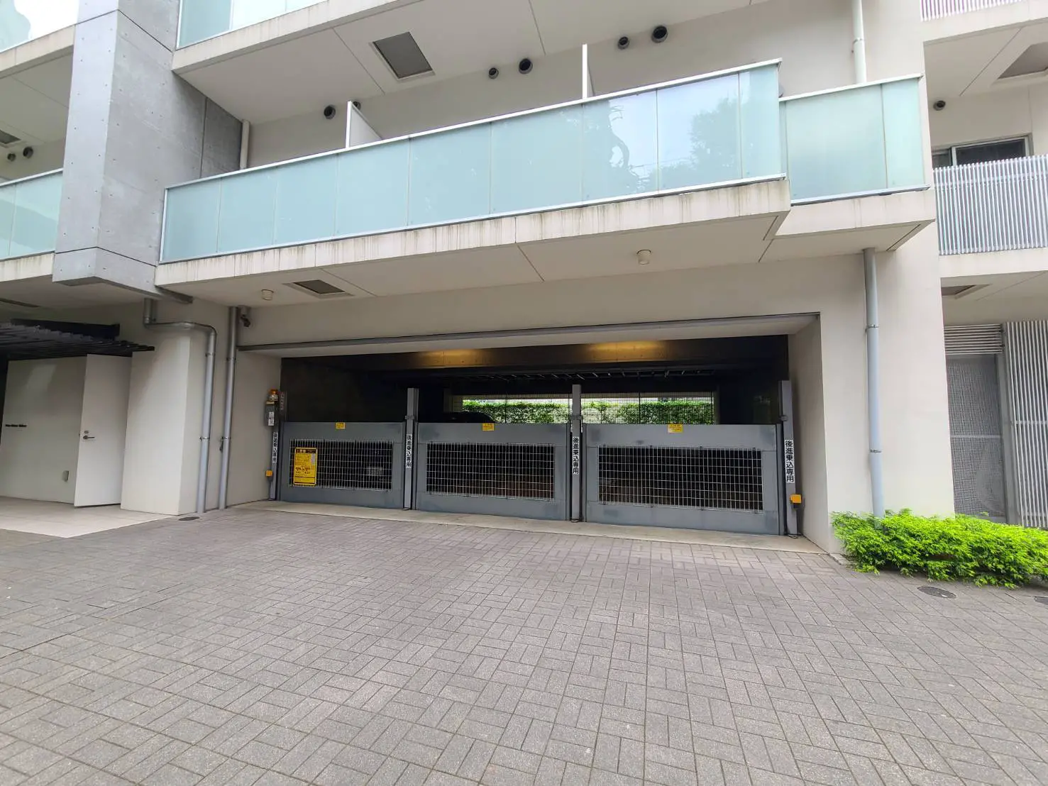 - モダンなマンションのエントランス、ガレージドアとガラスバルコニー、整然とした敷地の外観