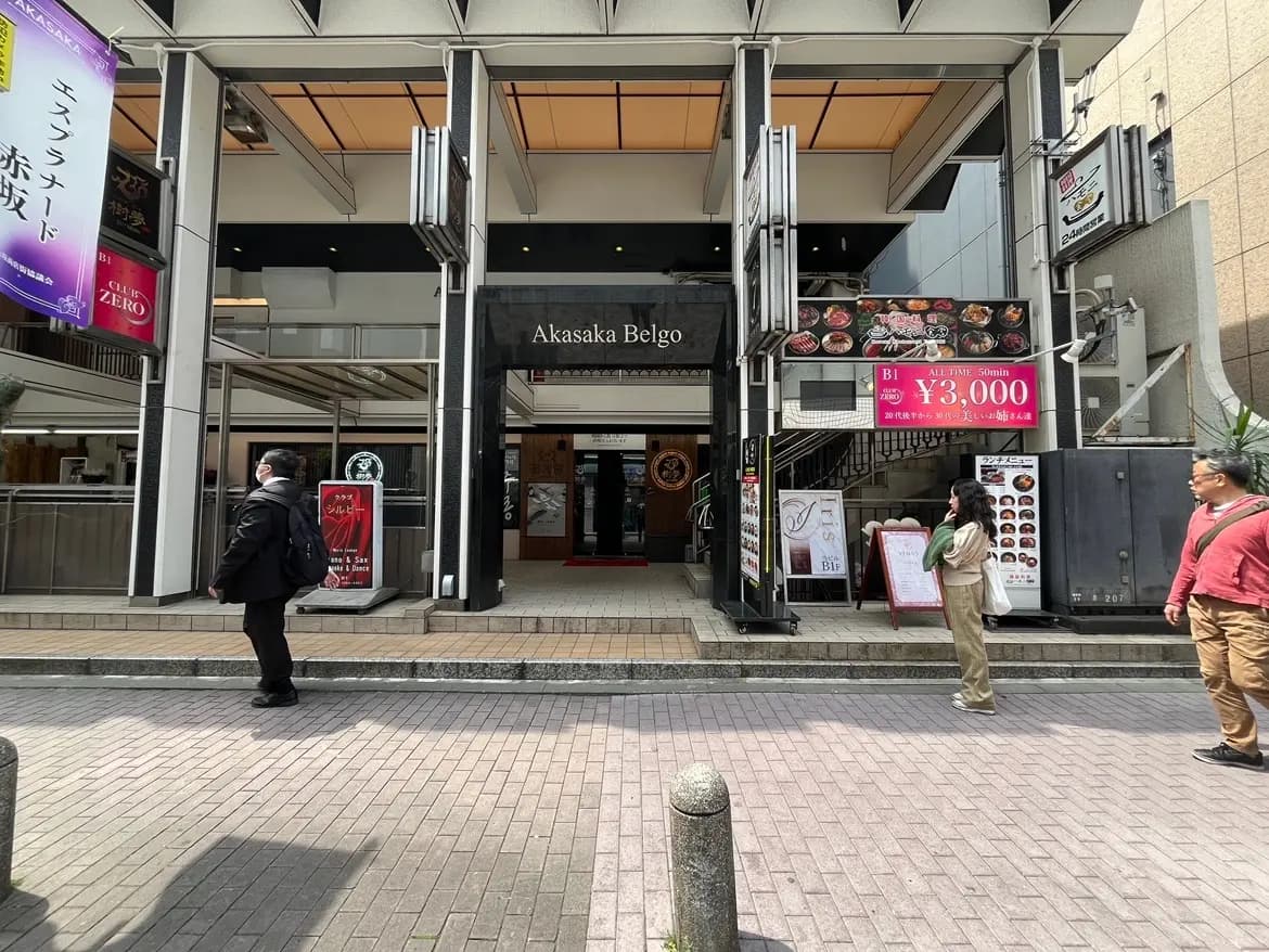 - 赤坂ベルゴの入り口、食事メニューの看板と賑やかな歩道が広がる商業区域の風景