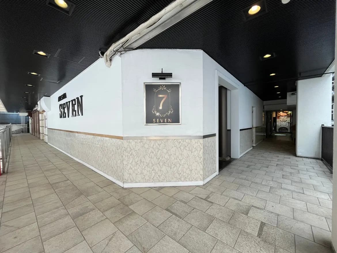 - モダンなデザインの商業ビルの通路、壁に「SEVEN」と書かれた看板とマーブル模様の装飾、明るい照明が施された入口付近の様子