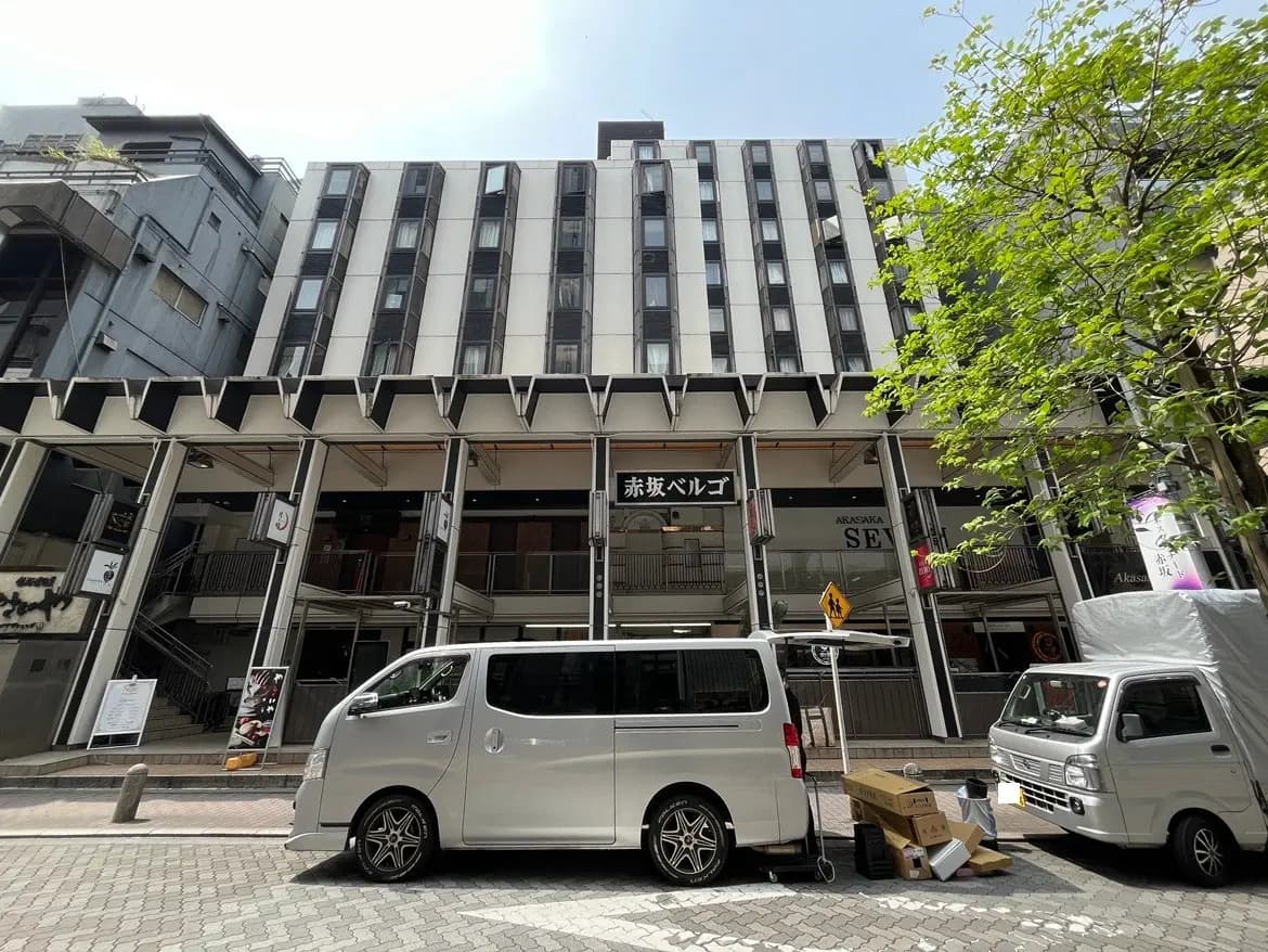 - 赤坂ベルゴの外観、モダンなデザインのビルと通りに停まるバン、周囲の緑と賑やかな街並み