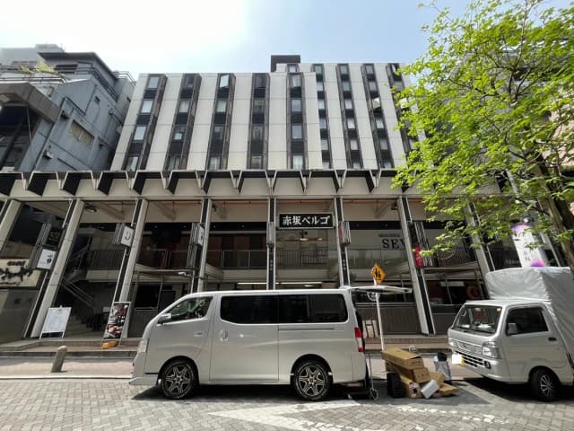 - 赤坂ベルゴの外観、モダンなデザインのビルと通りに停まるバン、周囲の緑と賑やかな街並み