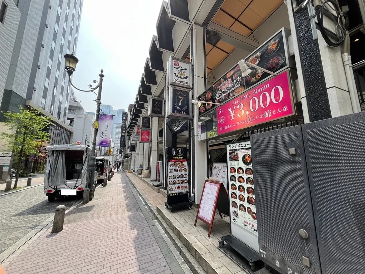 - 都心の飲食店街、看板にはランチメニューと金額が表示されており、歩道にはテーブルが並ぶ様子
