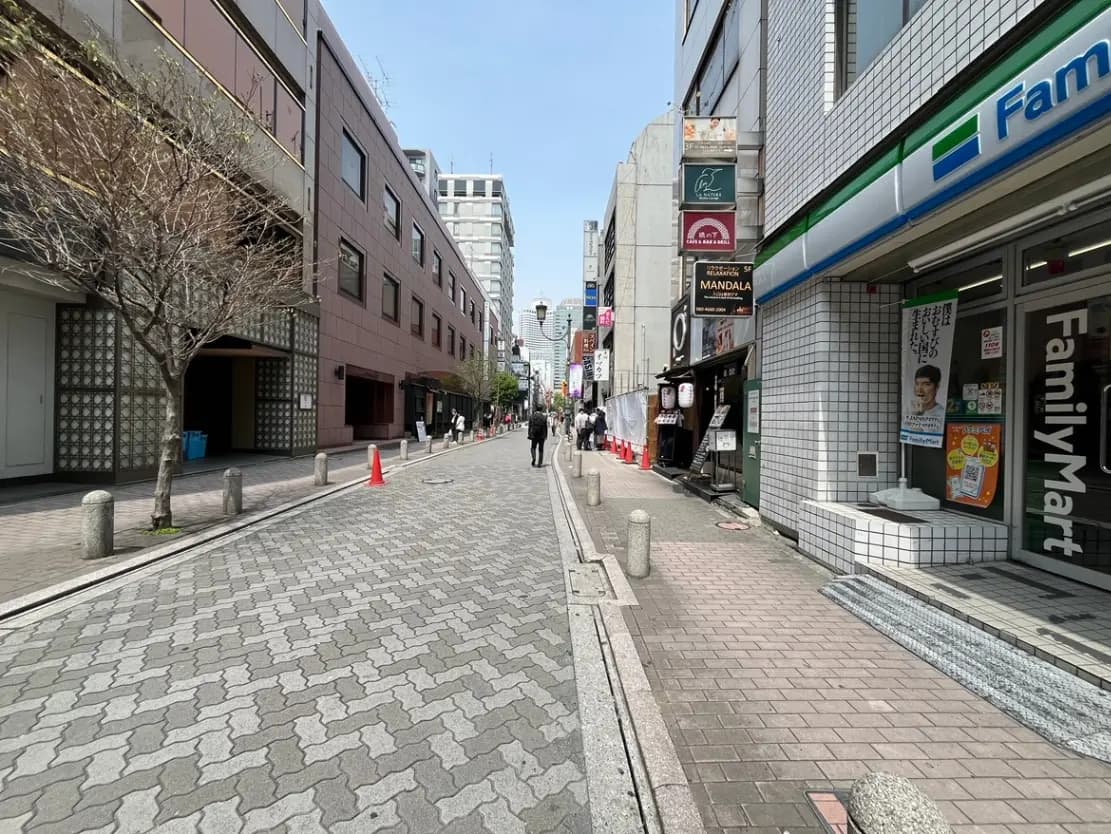 - 都市の通り、ファミリーマートと飲食店が並び、歩行者が行き交う賑やかな光景、木々が点在する景観