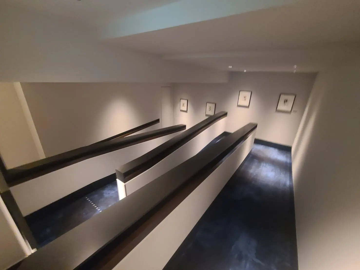 - モダンなデザインの廊下、直線的な手すりと照明が施された壁、美しいアートが飾られたインテリア