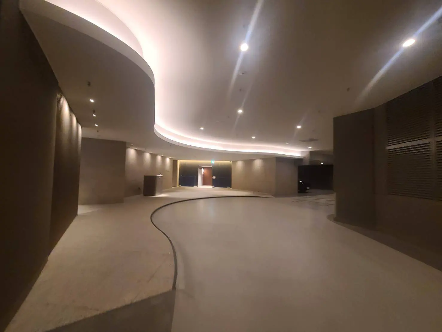 - モダンなデザインのロビー、曲線状の天井と間接照明が施された広々とした空間、落ち着いた色合いの壁と床が特徴のインテリア