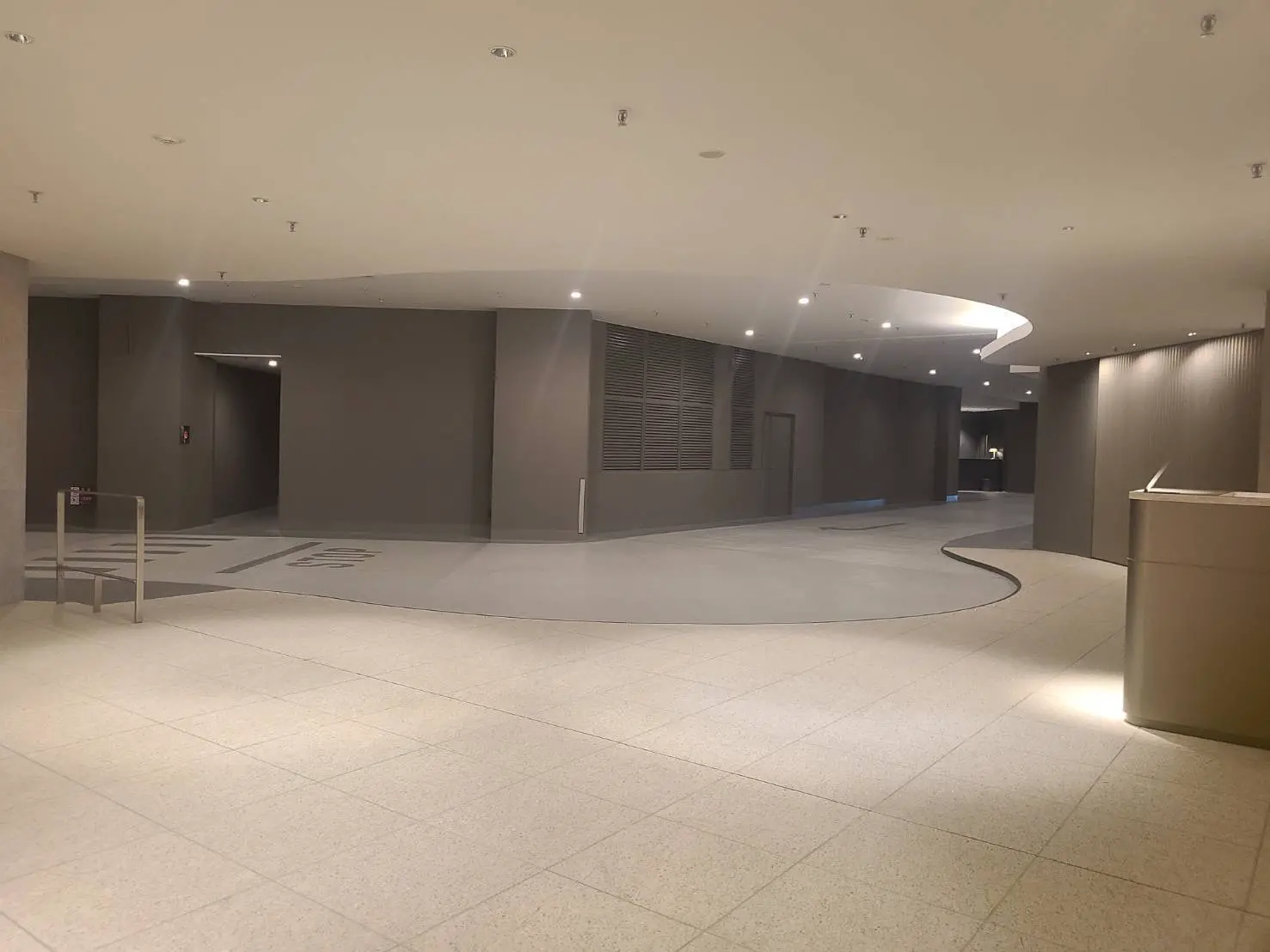 - モダンなデザインのロビー、滑らかな曲線の床と柔らかい照明、グレーの壁に囲まれた広々とした空間